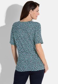 Kurzarmoberteil mit dunklem Hintergrund und kleinen blauen und grauen Blumenmustern, aus einem weichen Stoff gefertigt. Rundhals und entspannte Passform.