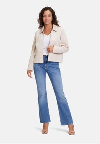 Beige, cropped jacka med spetsig krage och två framfickor, matchad med ljusblå utsvängda jeans. Slät tygtextur och enkel design.