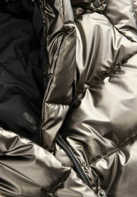 Metallic Puffer-Jacke mit Innenfutter, das eine glatte Textur, ein gestepptes Design und eine schwarze Innenverkleidung mit Reißverschluss und Druckknopfverschluss aufweist.