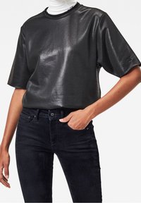 Svart, blänkande topp med korta ärmar och rund halsringning, matchad med mörka denimjeans. Tyget har en slät, glänsande yta.