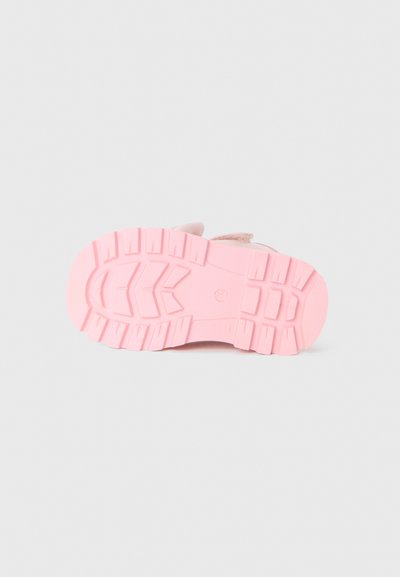 Semelle en caoutchouc rose d'une chaussure avec un motif texturé, offrant de profonds sillons et crêtes pour l'adhérence. Design épuré sans marquages visibles.