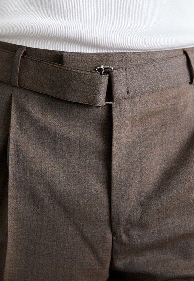 Pantalons marron sur mesure avec une texture lisse, présentant une taille plate, des passants de ceinture et un accent de boucle en argent à la taille.