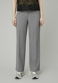 Pantalons anthracite ajustés à coupe droite, avec une texture lisse et un pli avant. Associés à des chaussures de sport argentées.