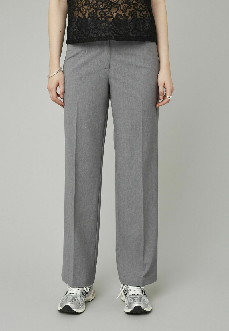 Pantalons anthracite ajustés à coupe droite, avec une texture lisse et un pli avant. Associés à des chaussures de sport argentées.
