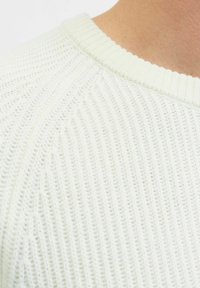 Maglione bianco a maglia con texture a coste, collo rotondo e una vista ravvicinata che mette in risalto il motivo e il dettaglio del tessuto.