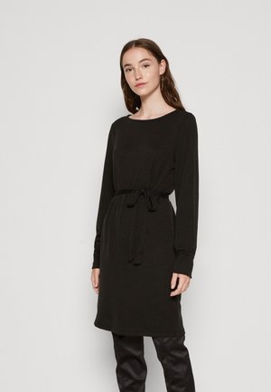 Svart strikket kjole med rund hals, lange ermer og knytedetalj i midjen. Stoffet har ribbestruktur, noe som gir et mykt utseende.