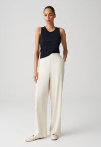 Top senza maniche nero, pantaloni bianchi a gamba larga e scarpe basse beige; texture lisce e linee pulite; palette di colori neutri.