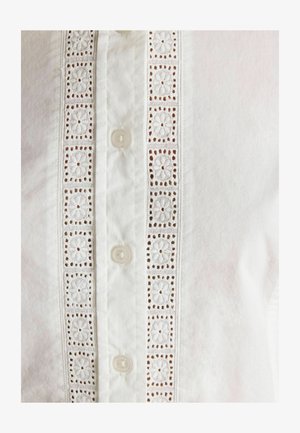 Weiße Bluse mit einer zentralen Knopfleiste, dekorativem Häkelspitzeneinsatz und bestickten Blumenmustern sowie kleinen Knopfverschlüssen.