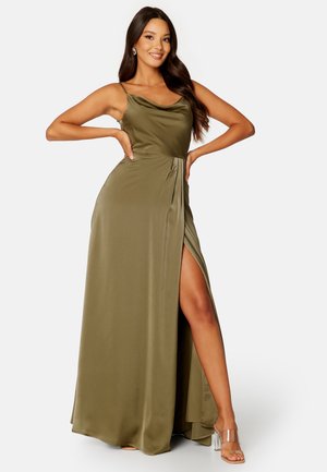 Maxi-jurk in olijfgroene satijn, met een cowl halslijn, een zijsplit, een flatterende drape en spaghettibandjes, gecombineerd met transparante hakken.
