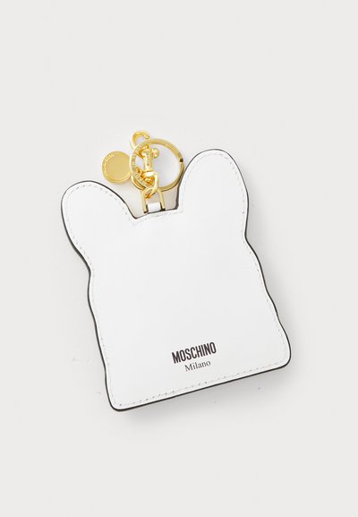 Portofel de chei din piele albă în formă de câine cu urechi rotunde, având margini negre, accesorii aurii și branding "Moschino Milano".
