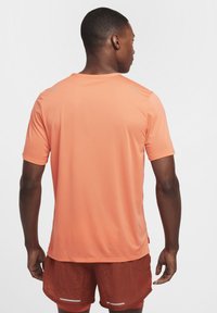 Camiseta deportiva de manga corta en un brillante color coral, hecha de una tela ligera con una textura suave. Contiene detalles reflectantes en los hombros.