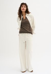 Giubbotto di jeans crema sopra un maglione marrone a scollo a V, abbinato a pantaloni larghi color crema. Tessuto strutturato con una vestibilità comoda e un design minimalista.