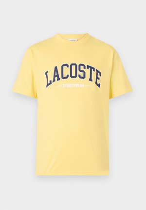 Gul bomull T-skjorte med marineblå "LACOSTE"-logo og "SPORTSWEAR"-tekst under. Enkel design med rund hals og korte ermer.