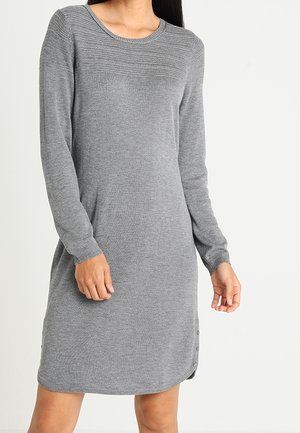 Femme portant une robe gris tricotée à manches longues et longueur genou, avec un subtil détail côtelé au niveau de l'encolure et des boutons sur l'ourlet latéral.
