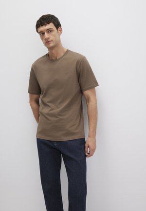 Braunes Baumwoll-T-Shirt mit runder Halslinie, kurzen Ärmeln und einem dezenten, gestickten Logo. Kombiniert mit blauen Jeans.