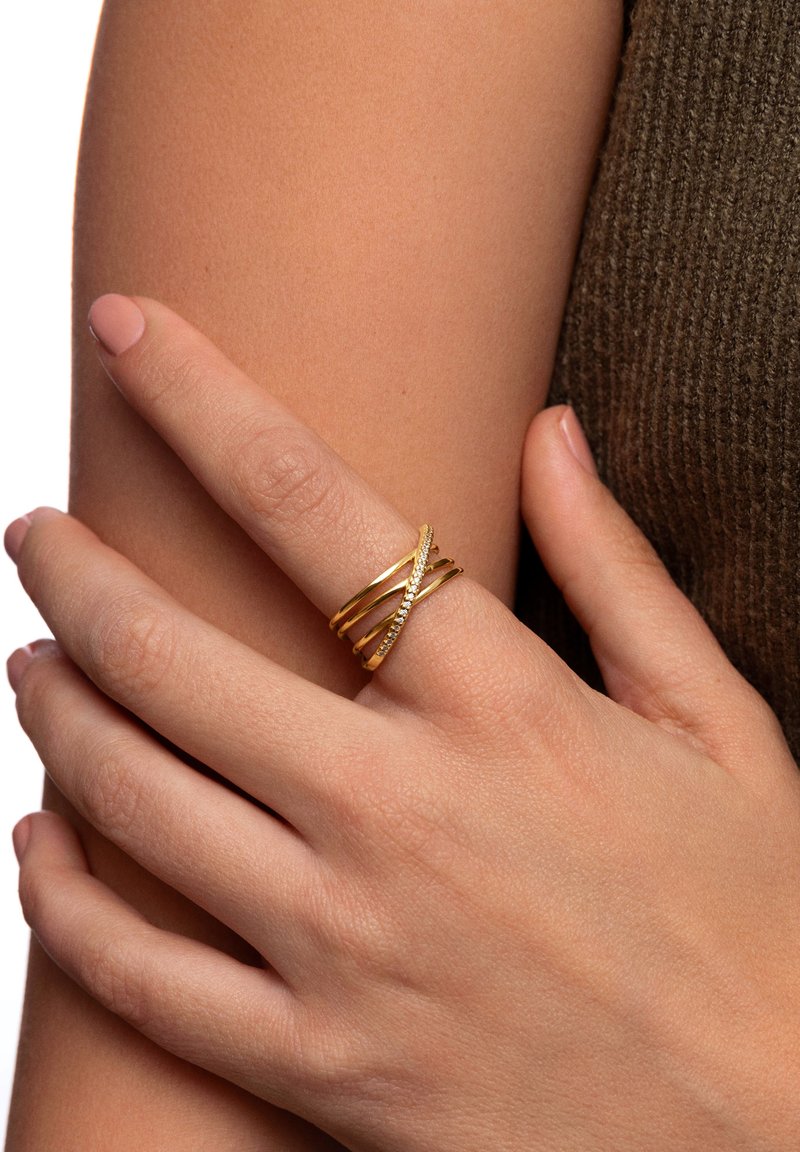Anello multibanda in oro con design intrecciati, finitura testurizzata e una banda decorata con piccole pietre trasparenti.