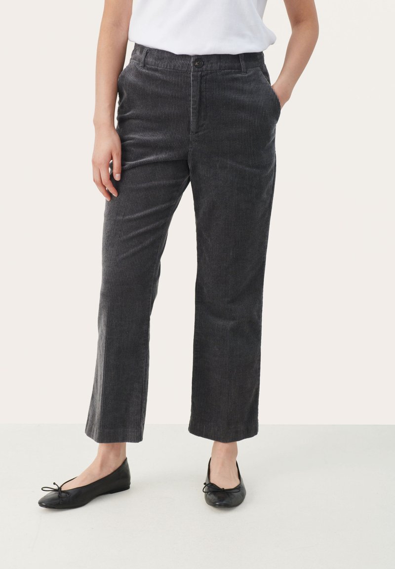 Pantalons en velours côtelé gris avec une coupe droite, dotés d'une fermeture à bouton visible et de poches, associés à des chaussures plates noires.