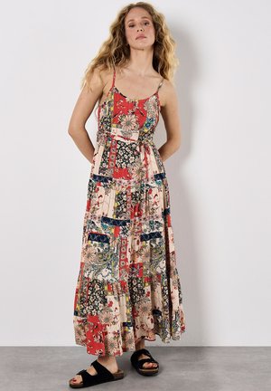 Maxikleid mit rot-blauem Patchworkdesign und floralen Motiven. Mit Spaghetti-Trägern und einem Kordelzug in der Taille. Getragen mit schwarzen Sandalen.