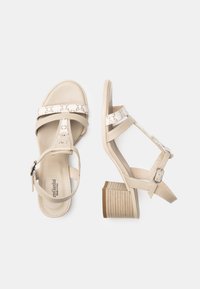 Beige heeled sandals with two wide straps, a patterned accent strap, and a textured heel. Buckle closure for adjustable fit.