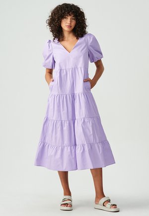 Vestido midi acampanado de color lavanda con mangas abullonadas, escote en forma de v y bolsillos laterales. Fabricado con una tela ligera y de textura suave.