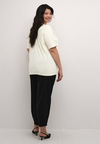 Light yellow short-sleeve shirt with a relaxed fit, paired with black, tapered pants. Heels are strappy, with a slight texture on the fabric.