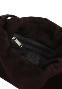 Dark brown suede bag interior with a black lining. Features a zip pocket and embossed logo patch. Soft texture, slouchy design.