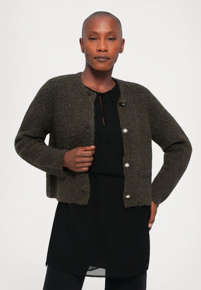 Brown textured cardigan with a round neckline and three transparent buttons. Worn over a black tunic with a drawstring detail.