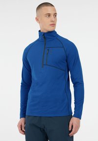 Modrá dlhá rukávová mikina na zips s vysokým golierom, textúrovaná tkanina a kontrastný čierny šev. Obsahuje zipsom uzatvárateľnú náprsníkovú kapsu.