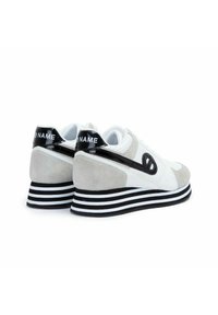 Witte en grijze sneakers met suède en leren accenten, gestreepte zwart-witte zool, ronde neus en logodetail op de hak.
