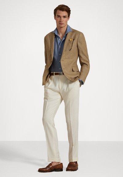 Bruine houndstooth blazer, lichtblauw overhemd, crèmekleurige broek, bruine leren schoenen. Een opvallend horloge en een zakdoek accentueren de outfit.