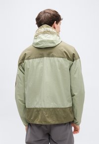 Ελαφρύ, δίχρωμο μπουφάν με κουκούλα σε απαλό πράσινο και ελιά. Διαθέτει άνετη εφαρμογή, απαλή υφή και λογότυπο Columbia στο λαιμό.