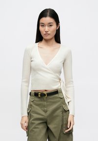 Top bej deschis cu dungi, tip wrap, cu decolteu adânc în V și mâneci lungi, având o fundă laterală. Asortat cu pantaloni cargo verde măsliniu.