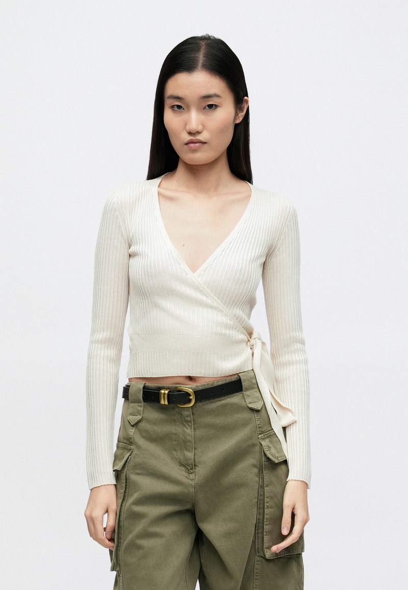 Top bej deschis cu dungi, tip wrap, cu decolteu adânc în V și mâneci lungi, având o fundă laterală. Asortat cu pantaloni cargo verde măsliniu.