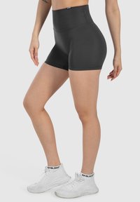 Pantalones cortos negros de cintura alta hechos de tela elástica, con una textura suave y un diseño sencillo. Llevados con zapatillas deportivas blancas.
