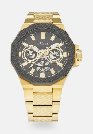Guld octagonal ur med en sort tekstureret skive, store guld timemarkeringsindekser og subskiver. Armbåndet har et vævet guld mønster.
