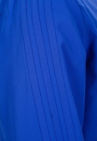 Leuchtend blauer Stoff mit strukturierten Streifen und dezenten Stickdetails, der eine glatte Oberfläche und ein sportliches Design zeigt.