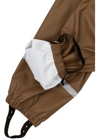I pantaloni impermeabili marroni presentano una tasca con apertura elastica in bianco. Una striscia riflettente grigia corre lungo il lato.