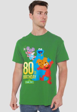 Grünes Baumwoll-T-Shirt mit bunten Charakteren aus der Sesamstraße, mit "80. GEBURTSTAG" in fetter gelber Schrift.
