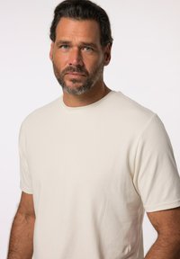 Crème-kleurige katoenen t-shirt met een ronde hals en korte mouwen. Zachte textuur, relaxte pasvorm en geen zichtbare patronen of versieringen.