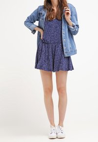 Robe bleu et blanche à pois, avec une jupe évasée, associée à une veste en denim légère. Des baskets blanches complètent le look décontracté.