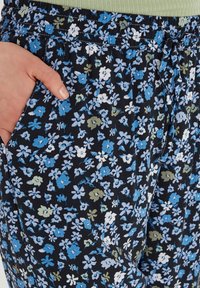 Pantaloni a fiori blu, bianchi e verdi su sfondo nero, con vita elastica e tasche laterali.