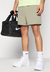 Γκρι αθλητικά σορτς, μαύρη τσάντα duffel Nike, λευκά αθλητικά παπούτσια και κάλτσες με μαύρα λογότυπα. Ομαλό ύφασμα, άνετη εφαρμογή και αντιθετικά χρώματα.