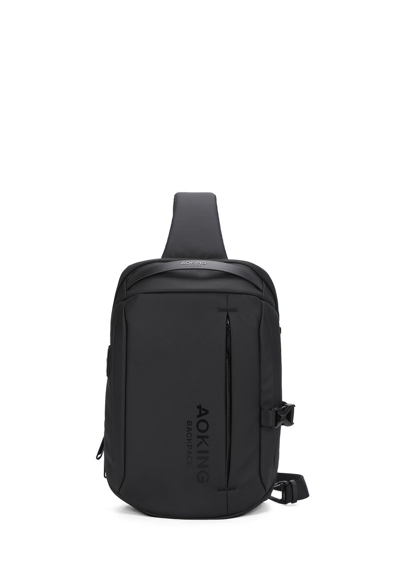 Zaino a tracolla nero realizzato in tessuto liscio, dotato di tasca frontale con zip, strap regolabile e logo del marchio stampato in verticale.
