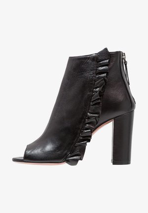 Bottine en cuir noir à talon haut, bout ouvert, détail volanté le long du côté extérieur, et fermeture éclair à l'arrière.