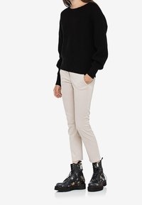 Svart stickad tröja med sänkta axlar, beige åtsittande byxor och blommönstrade svarta kängor med snörningsdetalj.