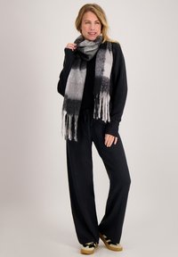 Zwart-grijs ombre sjaal met franjes aan de uiteinden, gedragen over een zwarte outfit. De sjaal is zacht, met een verloopontwerp en een lichte textuur.