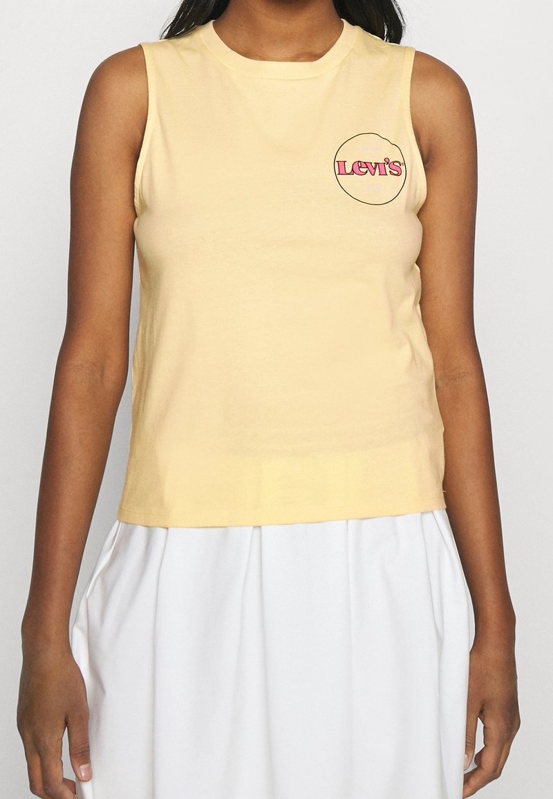 Gul ärmlös bomullstop med en rund Levi's-logotyp i rosa och svart framtill, med rund halsringning och en figurnära silhuett.
