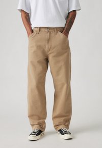 Bež hlače iz bombažnega keperja z ravnim krojem, z bočnimi žepi, sprednjo zaponko na gumbe in vidnimi šivi.