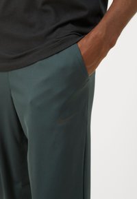 Spodnie sportowe Nike w ciemnozielonym kolorze, o eleganckim designie, gładkiej teksturze, bocznych kieszeniach i dyskretnym czarnym logo na udzie.