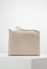 Pochette in pelle beige con texture liscia, chiusura con zip e cinturino da polso. Design rettangolare minimalista senza elementi in metallo visibili.